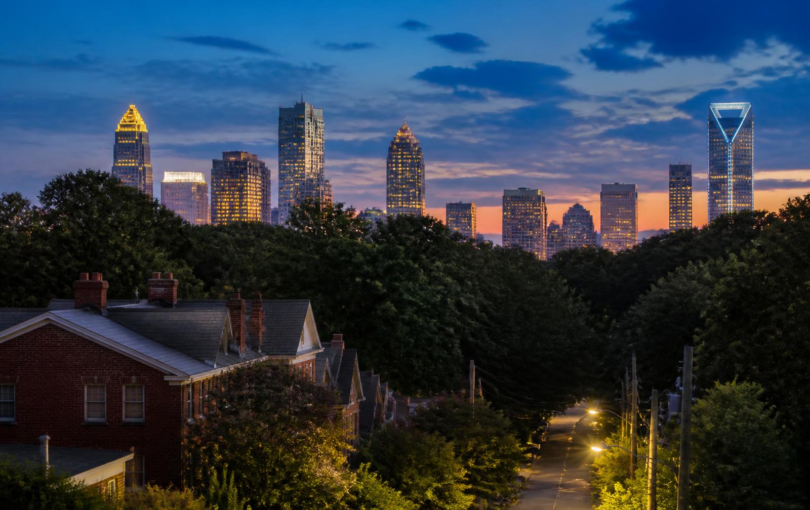 Charlotte skyline at dusk seen beyond the oak canopy of a residential street